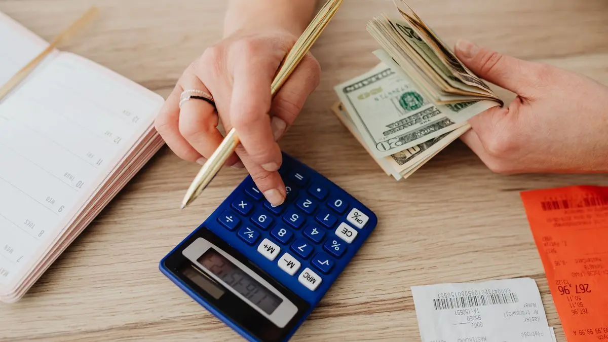 Manos manejando efectivo y una calculadora para planificar el presupuesto escolar